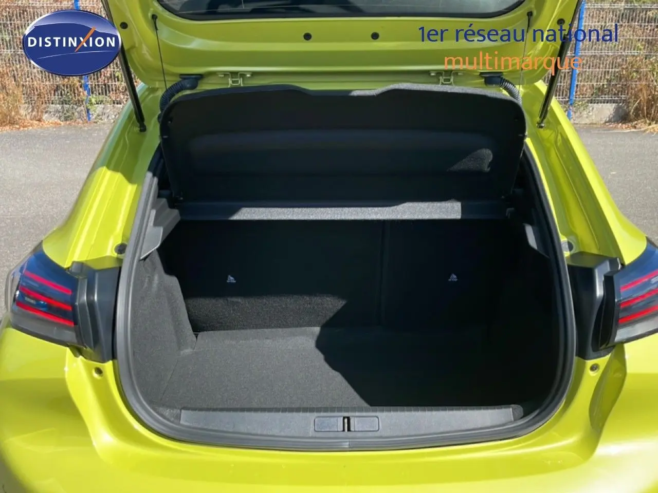 Coffre ouvert vu de l'arrière d'une Peugeot 208 hybride jaune Agueda Metal, avec feux arrière LED visibles.
