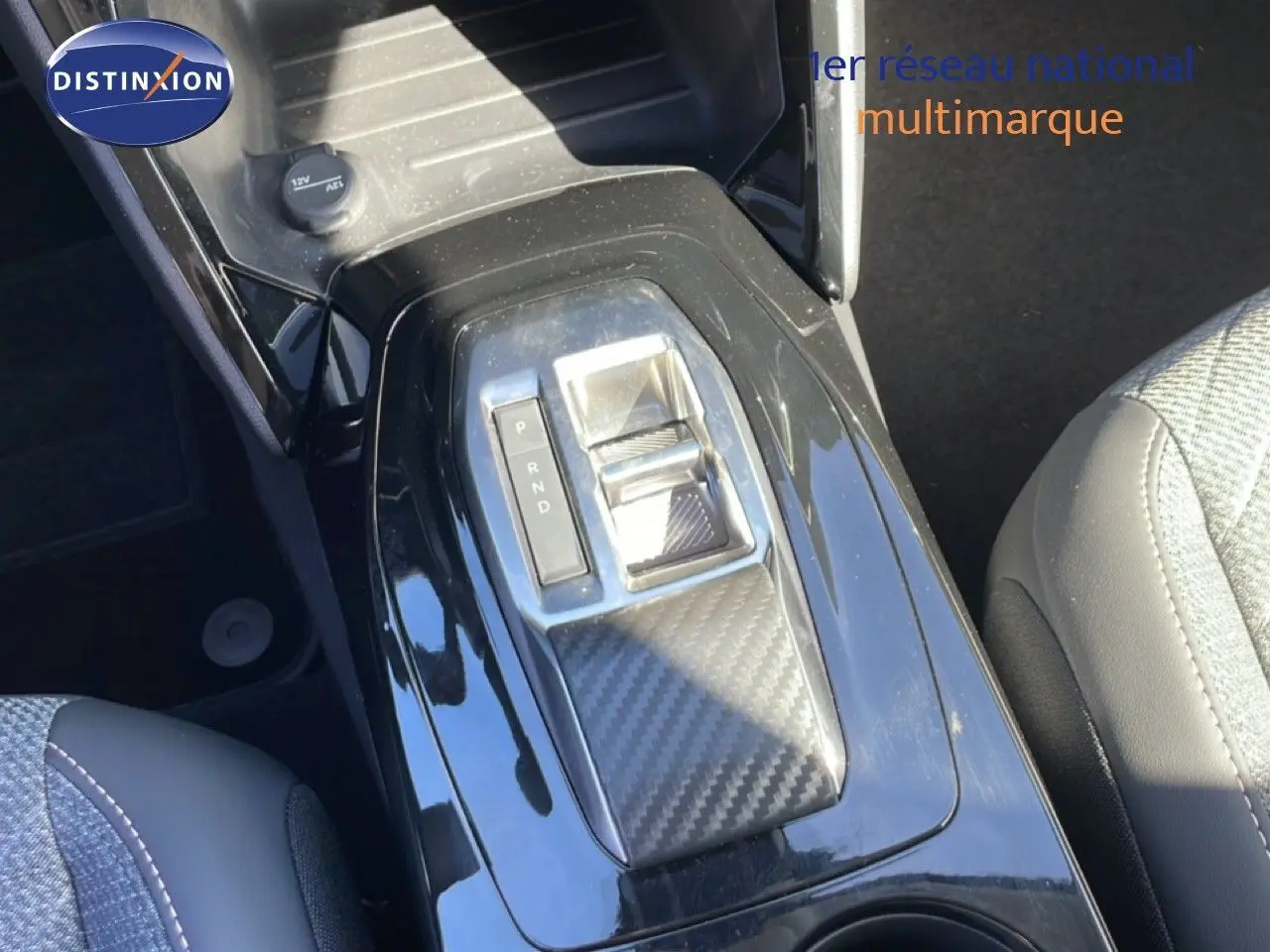 Gros plan sur la console centrale de la Peugeot 208 Hybrid 110ch, avec levier de boîte auto et finition carbone noire.