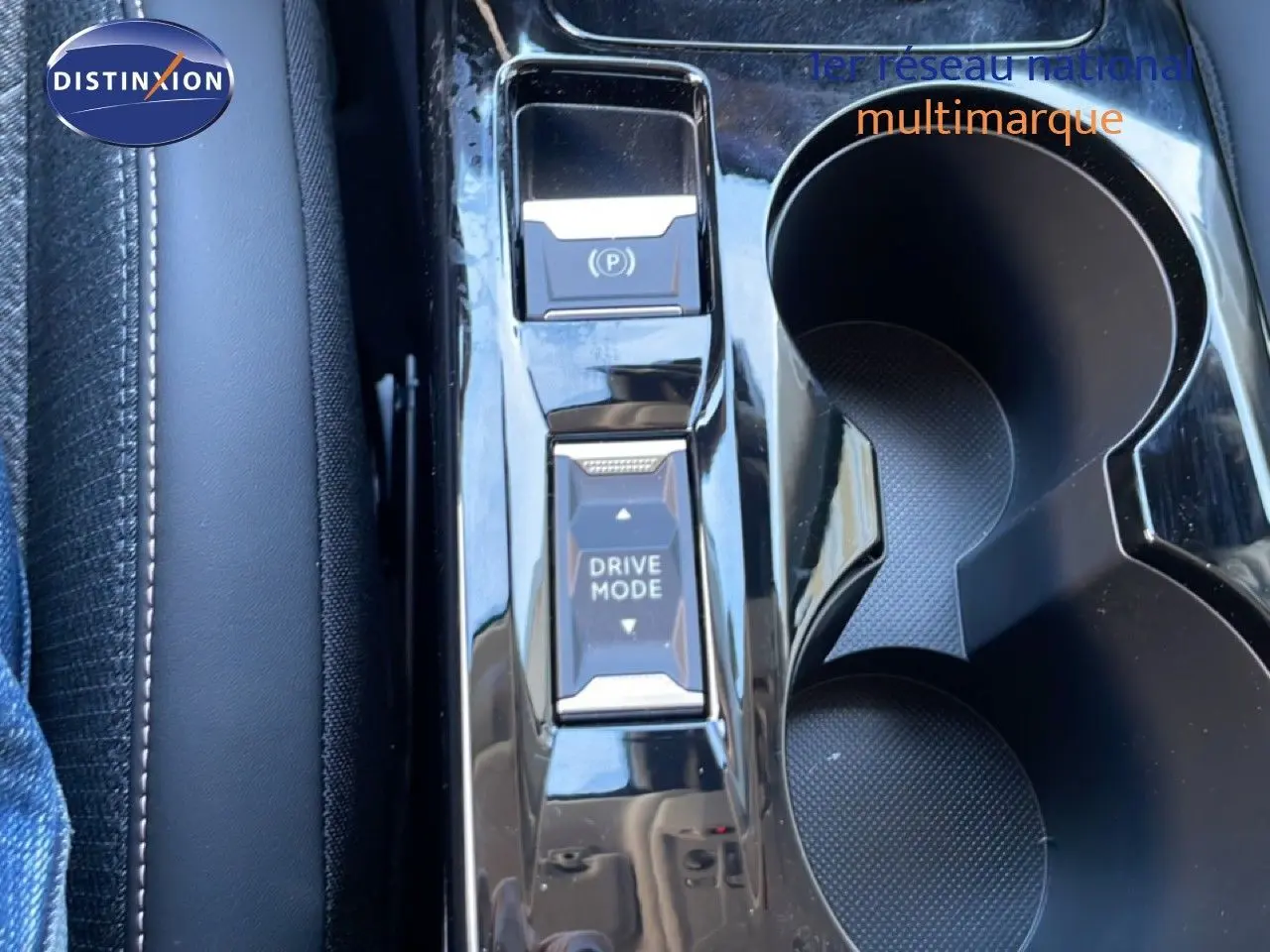 Gros plan sur la console centrale noire brillante de la Peugeot 208 Hybrid 110ch, avec boutons Drive Mode et frein à main électrique.