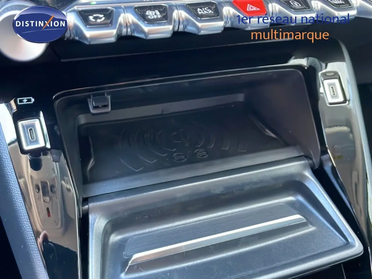 Gros plan sur la console centrale noire du Peugeot 208 Hybrid 110ch, montrant le compartiment de recharge sans fil et ports USB.