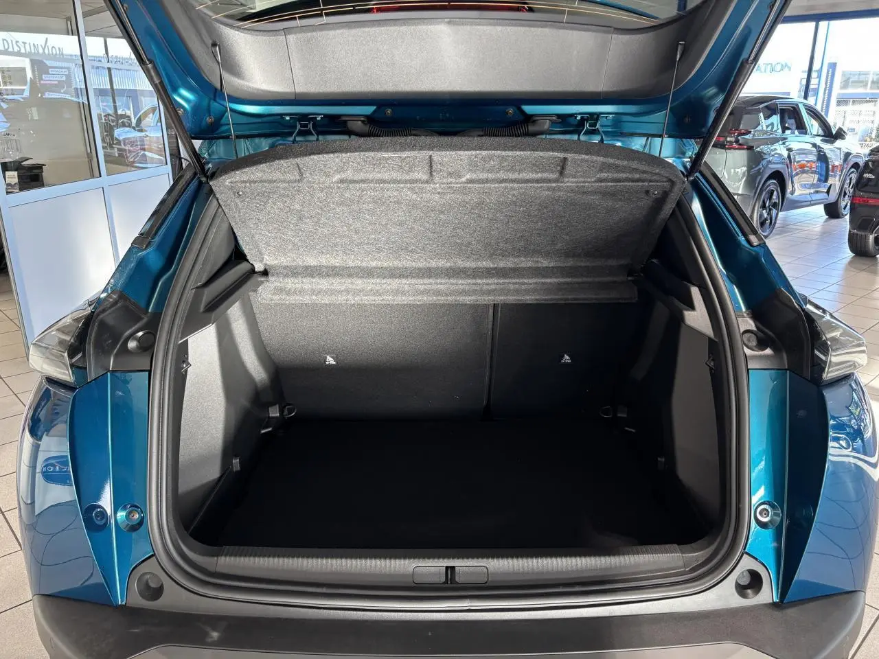 Coffre ouvert vu de l'arrière du Peugeot 2008 bleu, montrant l'espace de chargement et la trappe intérieure grise.