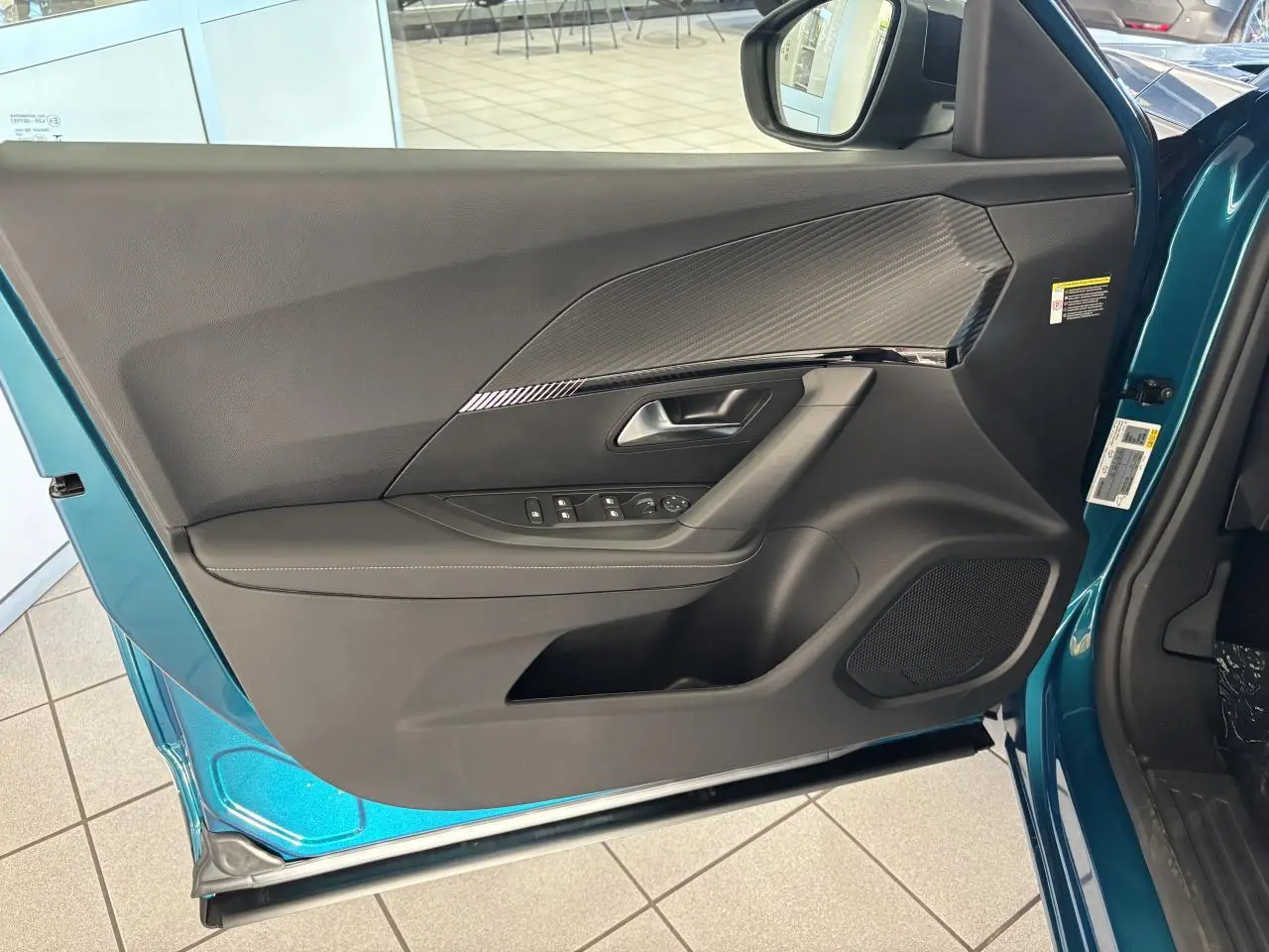 Vue intérieure de la porte avant gauche bleu métallisé du Peugeot 2008 avec insert carbone et haut-parleur intégré.