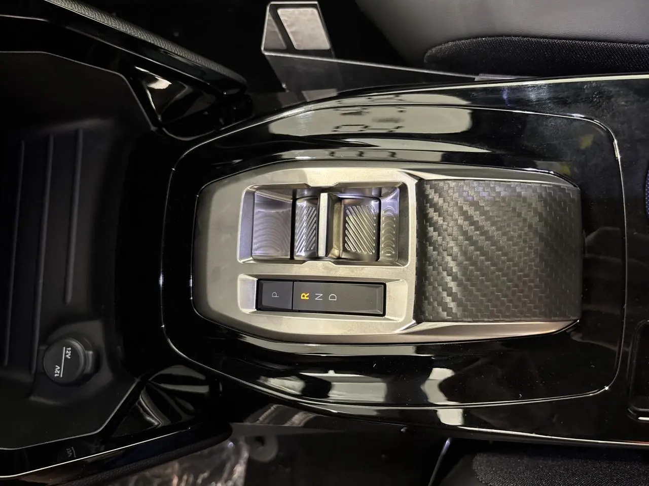 Vue plongeante sur la console centrale noire brillante du Peugeot 2008 hybride avec sélecteur de boîte automatique en carbone.
