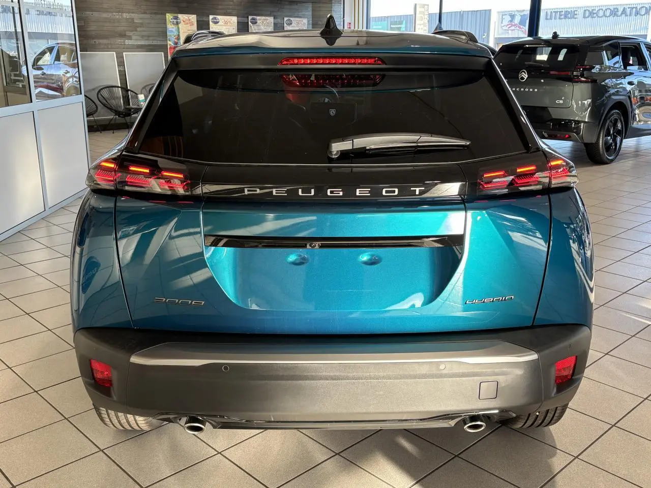 Vue arrière d'un Peugeot 2008 hybride bleu métallisé avec feux arrière LED en forme de griffes et double sortie d'échappement chromée.