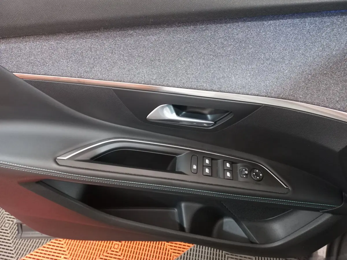 Gros plan sur la porte côté conducteur du Peugeot 5008 gris foncé, montrant les commandes des vitres et la poignée intérieure.