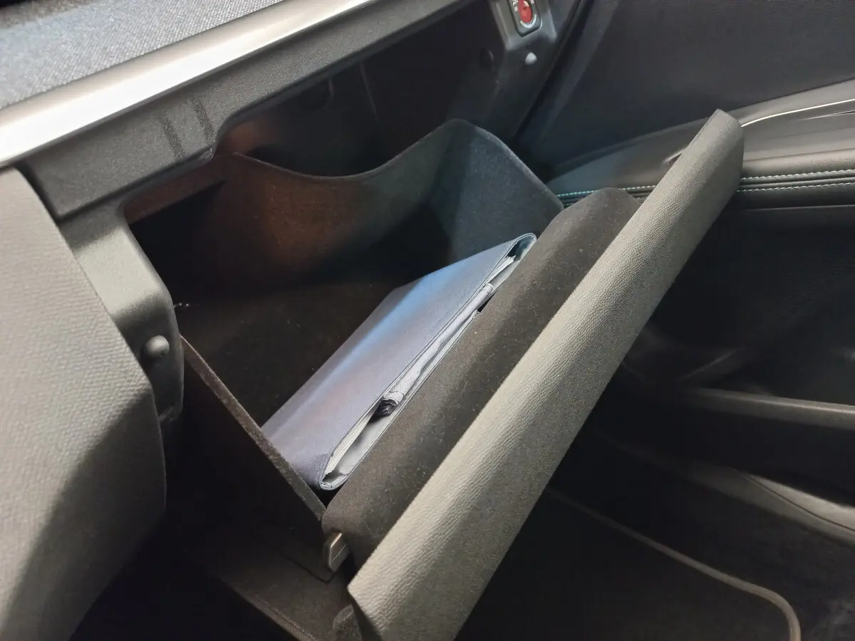 Gros plan sur la boîte à gants ouverte du Peugeot 5008 gris foncé, montrant un carnet de bord à l'intérieur.
