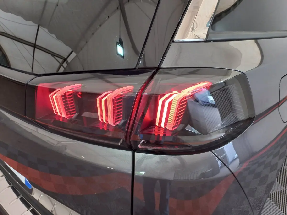 Gros plan sur les feux arrière allumés côté gauche d'un Peugeot 5008 gris foncé dans un garage.