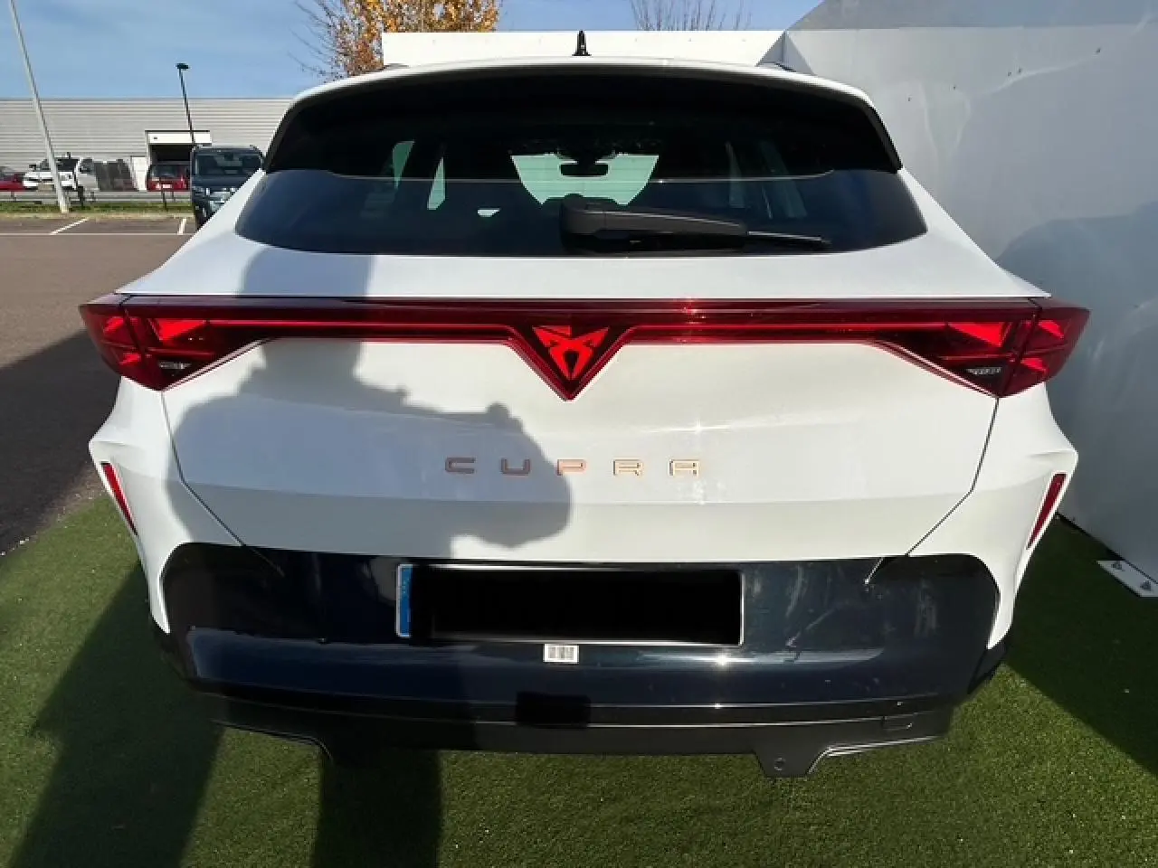 Vue arrière d'une CUPRA Formentor blanc neige avec bandeau lumineux rouge et logo CUPRA éclairé au centre.