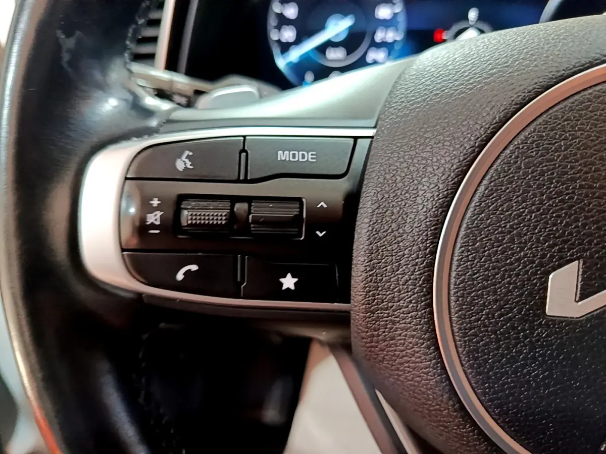 Gros plan sur les commandes gauche du volant cuir noir du KIA SPORTAGE blanc 2022 avec affichage numérique en arrière-plan.