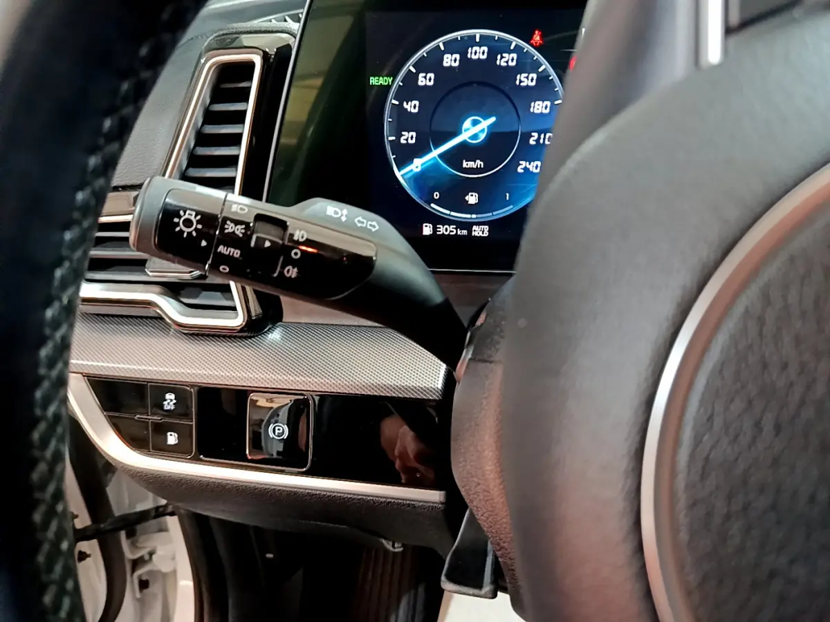 Vue intérieure rapprochée du tableau de bord et volant du KIA SPORTAGE blanc, affichage digital du compteur et commandes lumineuses.