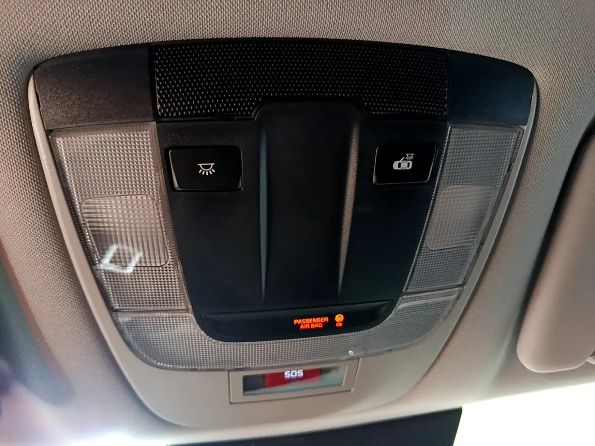 Vue rapprochée du panneau de commande au plafond intérieur du Kia Sportage blanc 2022 avec bouton SOS et indicateur airbag passager.