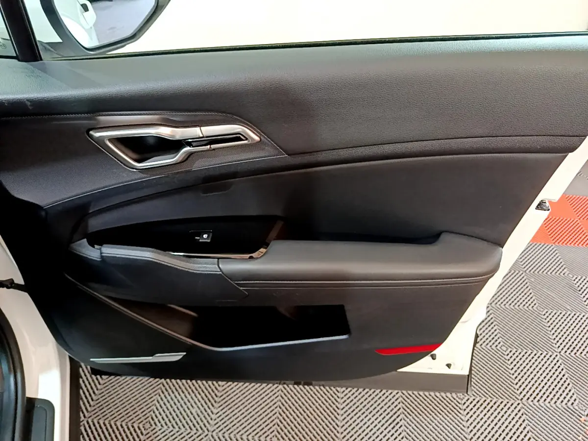 Intérieur côté gauche de la porte avant blanche du Kia Sportage 2022 avec poignée argentée et panneau noir.