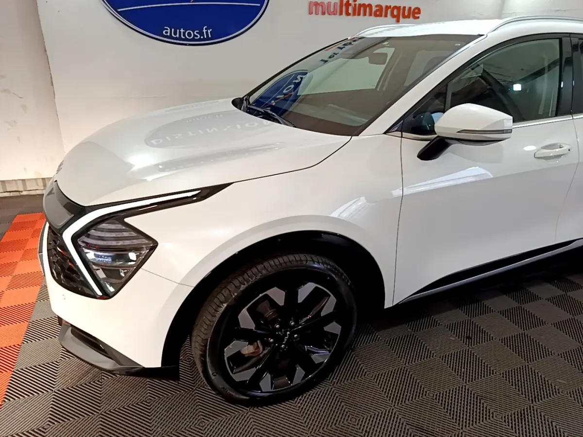 Vue 3/4 avant droit du KIA SPORTAGE blanc avec jantes noires et feux LED en forme de boomerang.