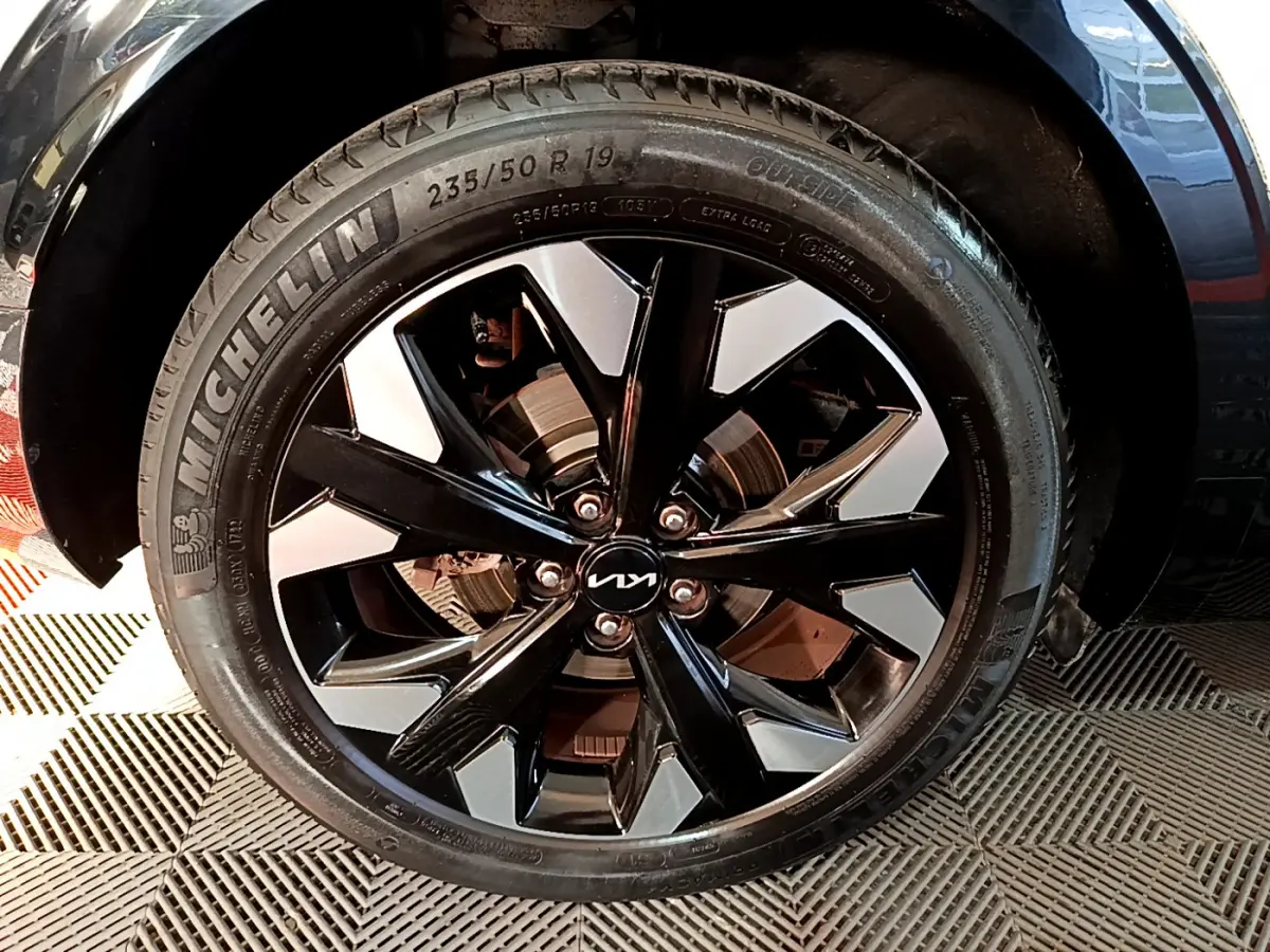 Gros plan sur la roue avant droite du KIA SPORTAGE blanc, jante alliage noir et argent avec logo KIA central.