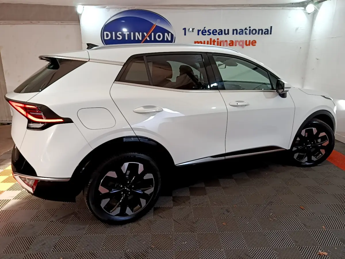 KIA SPORTAGE blanc en vue profil côté gauche, avec jantes noires et feux arrière LED allumés dans un showroom.