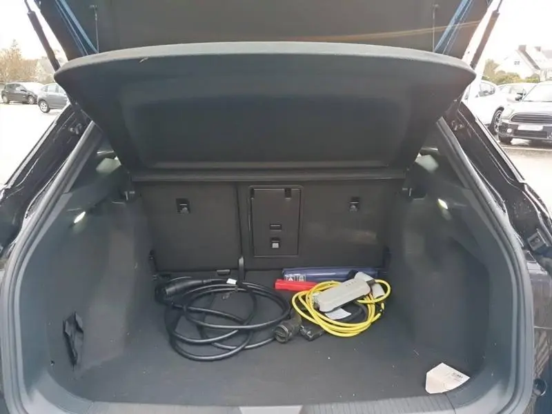 Coffre ouvert vu de l'arrière d'un Volkswagen ID.4 noir Ebène avec câbles de recharge électrique visibles.