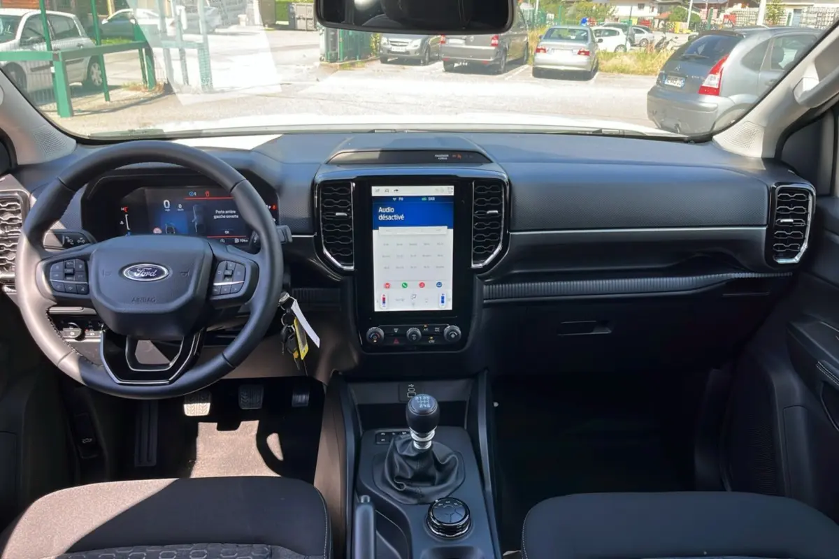 Vue intérieure avant du Ford Ranger 2026, tableau de bord noir avec écran tactile vertical et levier de vitesses manuel.