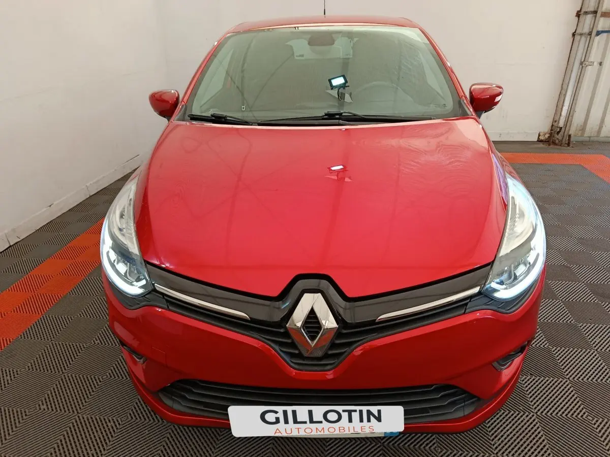 Vue frontale rapprochée d'une Renault Clio Intens rouge avec phares LED allumés dans un garage.