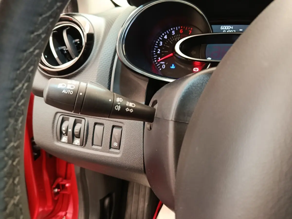 Vue intérieure côté gauche du volant de la Renault Clio rouge, avec commandes d'éclairage et tableau de bord partiel.
