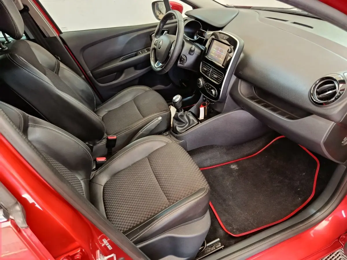 Vue intérieure côté conducteur de la Renault Clio Intens rouge, montrant sièges noirs et tableau de bord avec écran tactile.