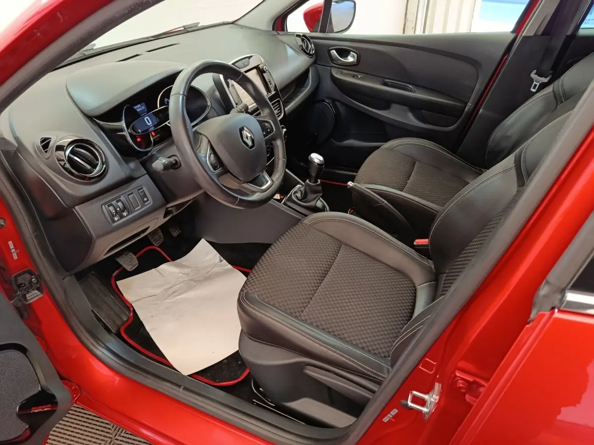 Vue intérieure côté conducteur de la Renault Clio rouge 2018, avec volant cuir et boîte manuelle visible.