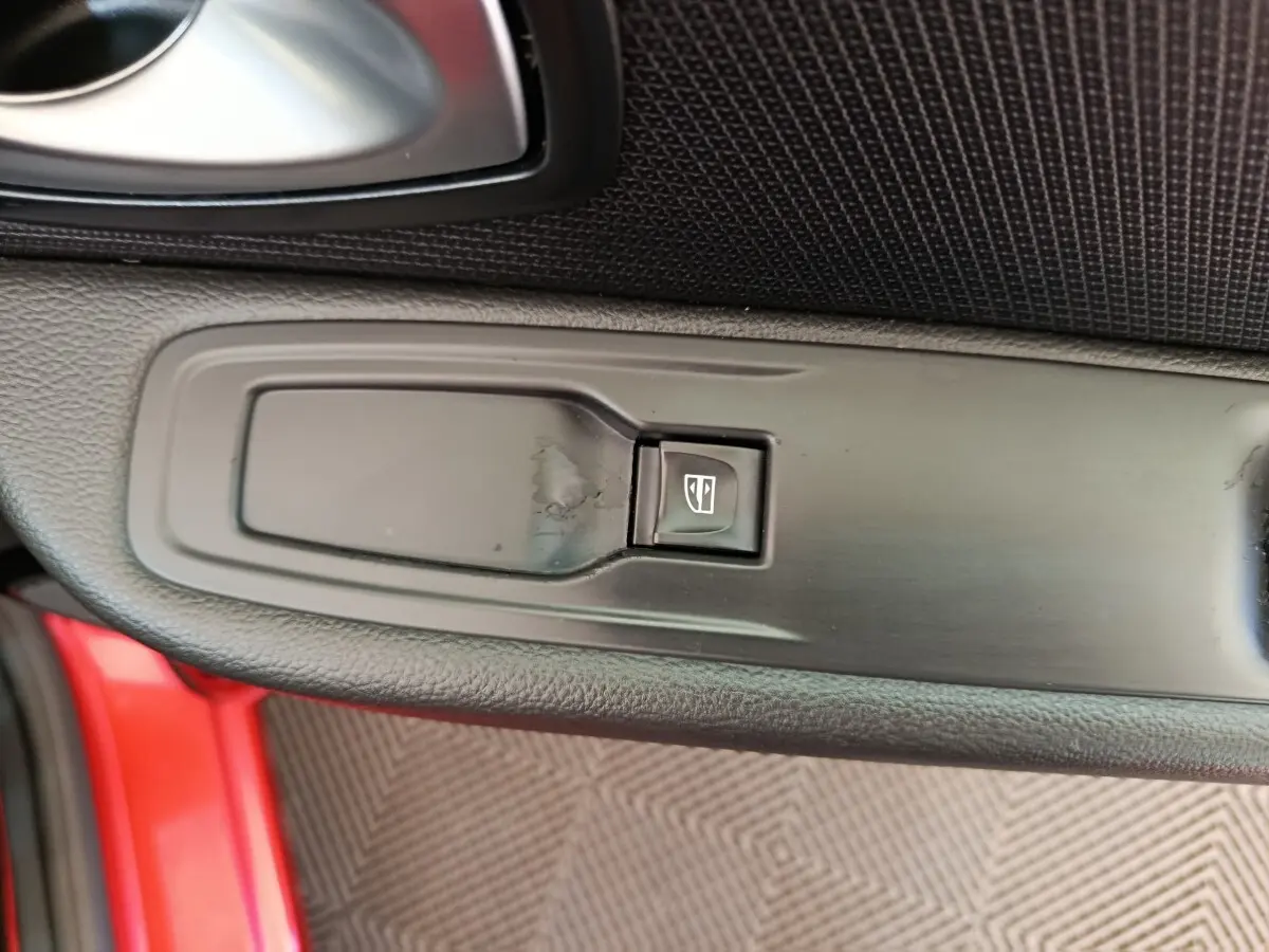 Gros plan sur le bouton de commande de la vitre électrique côté conducteur d’une Renault Clio rouge.