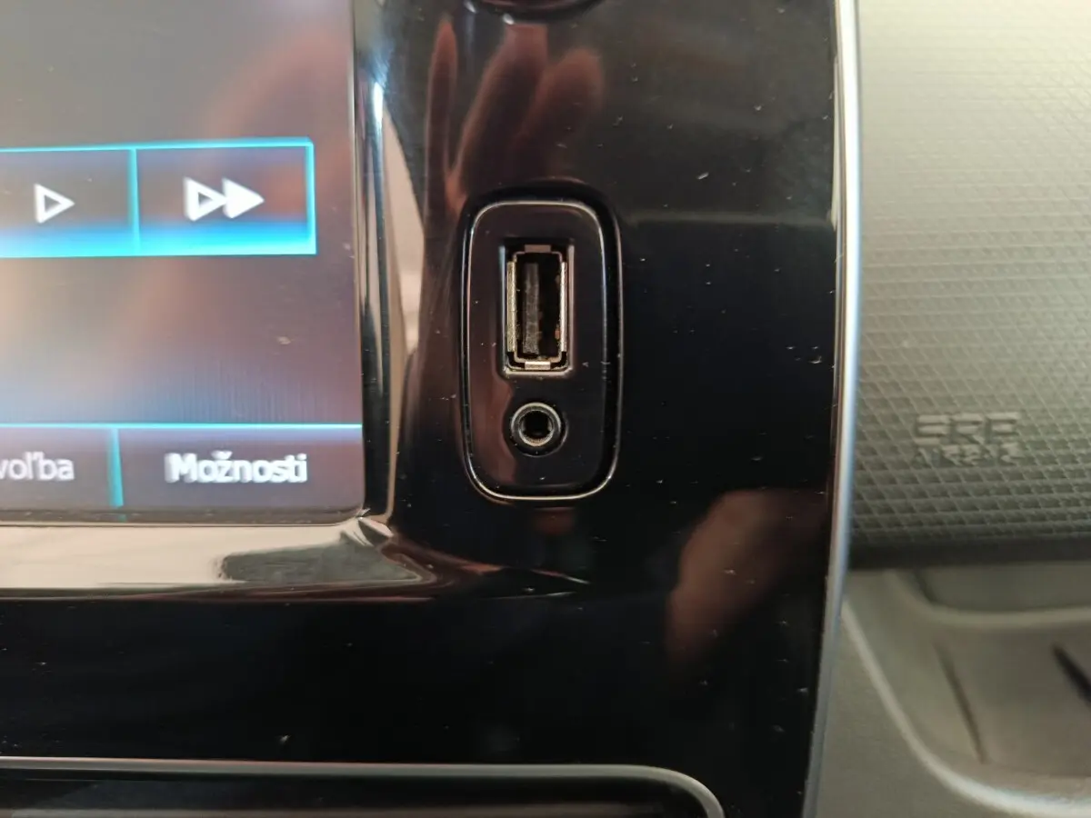 Gros plan sur la prise USB et prise jack intégrées à la console centrale noire d'une Renault Clio Intens rouge.