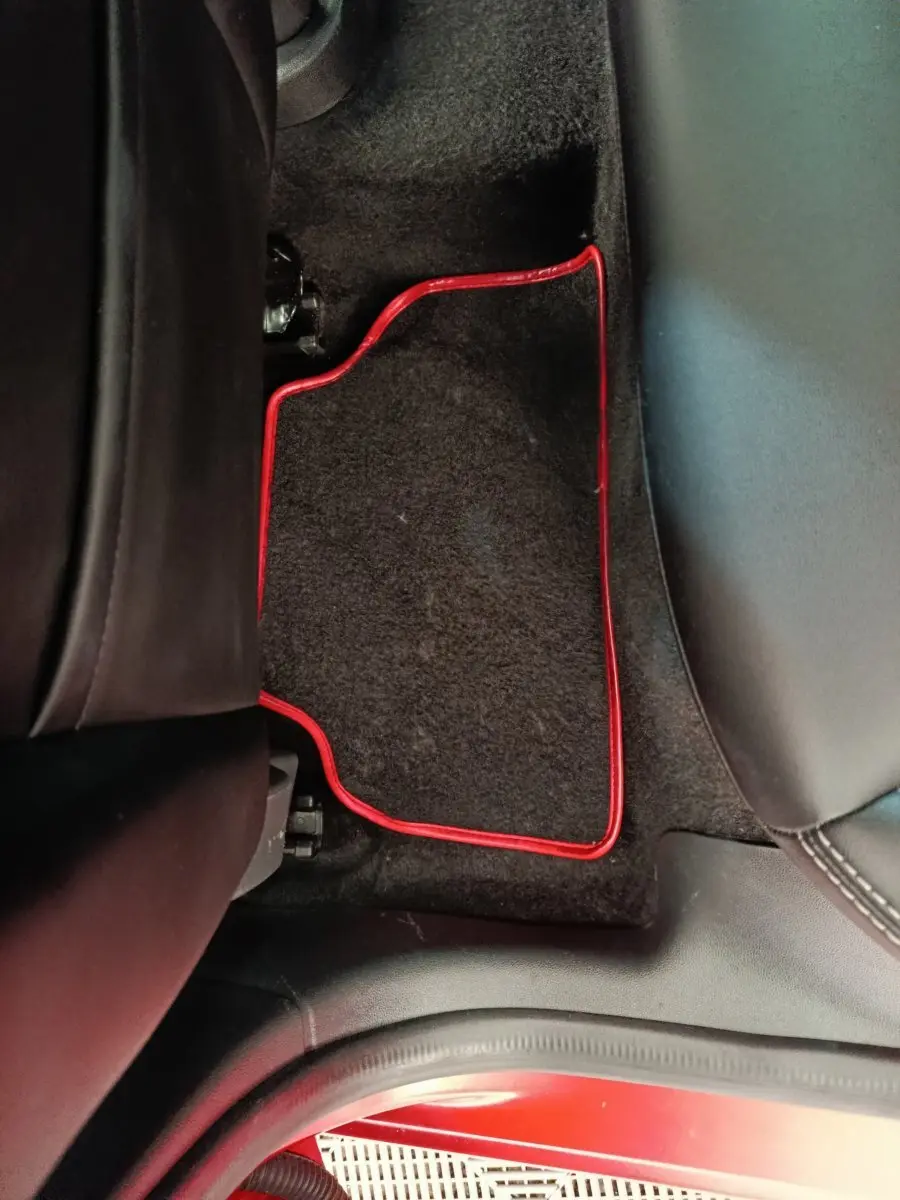 Détail du tapis de sol arrière noir avec bordure rouge dans une Renault Clio Intens rouge, vue intérieure côté gauche.