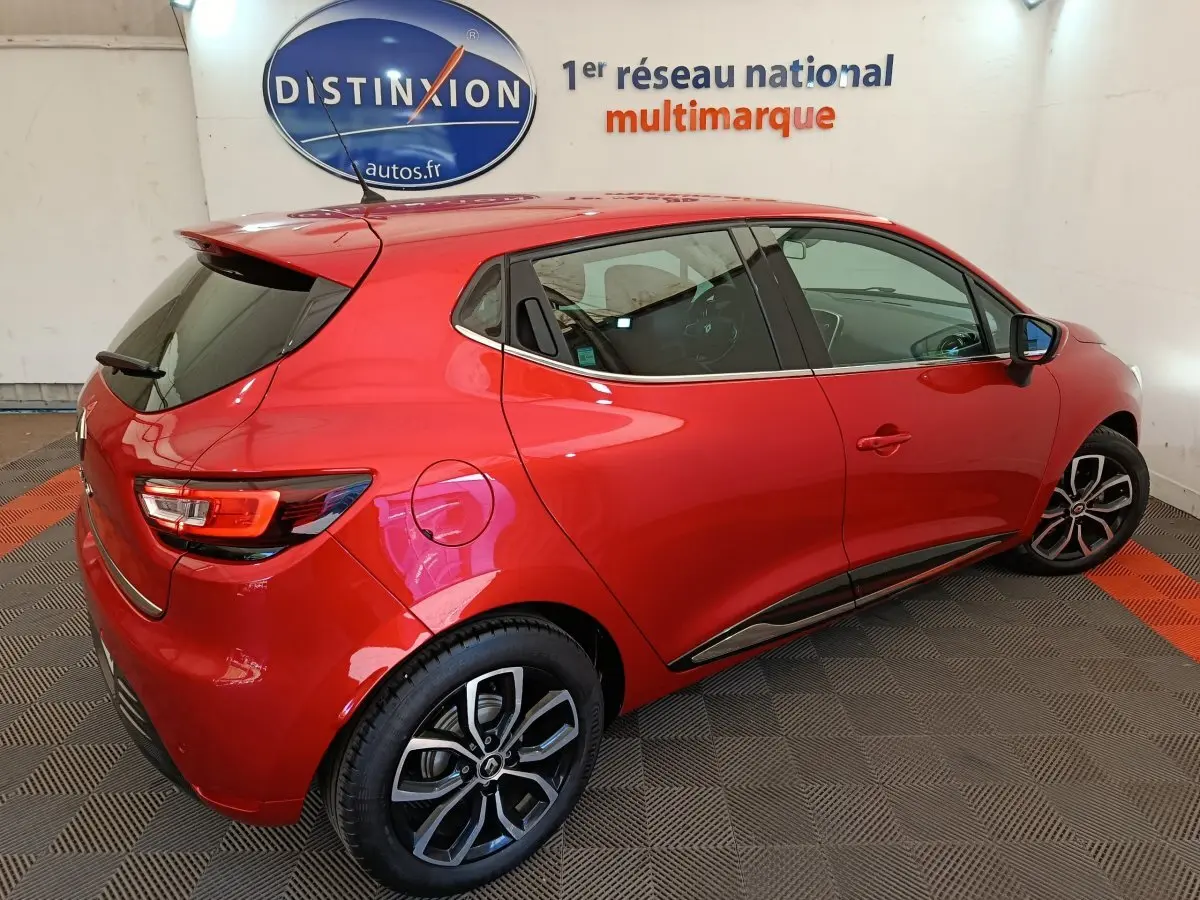 Renault Clio Intens rouge vue 3/4 arrière droit, avec jantes alliage et toit spoiler en intérieur showroom.