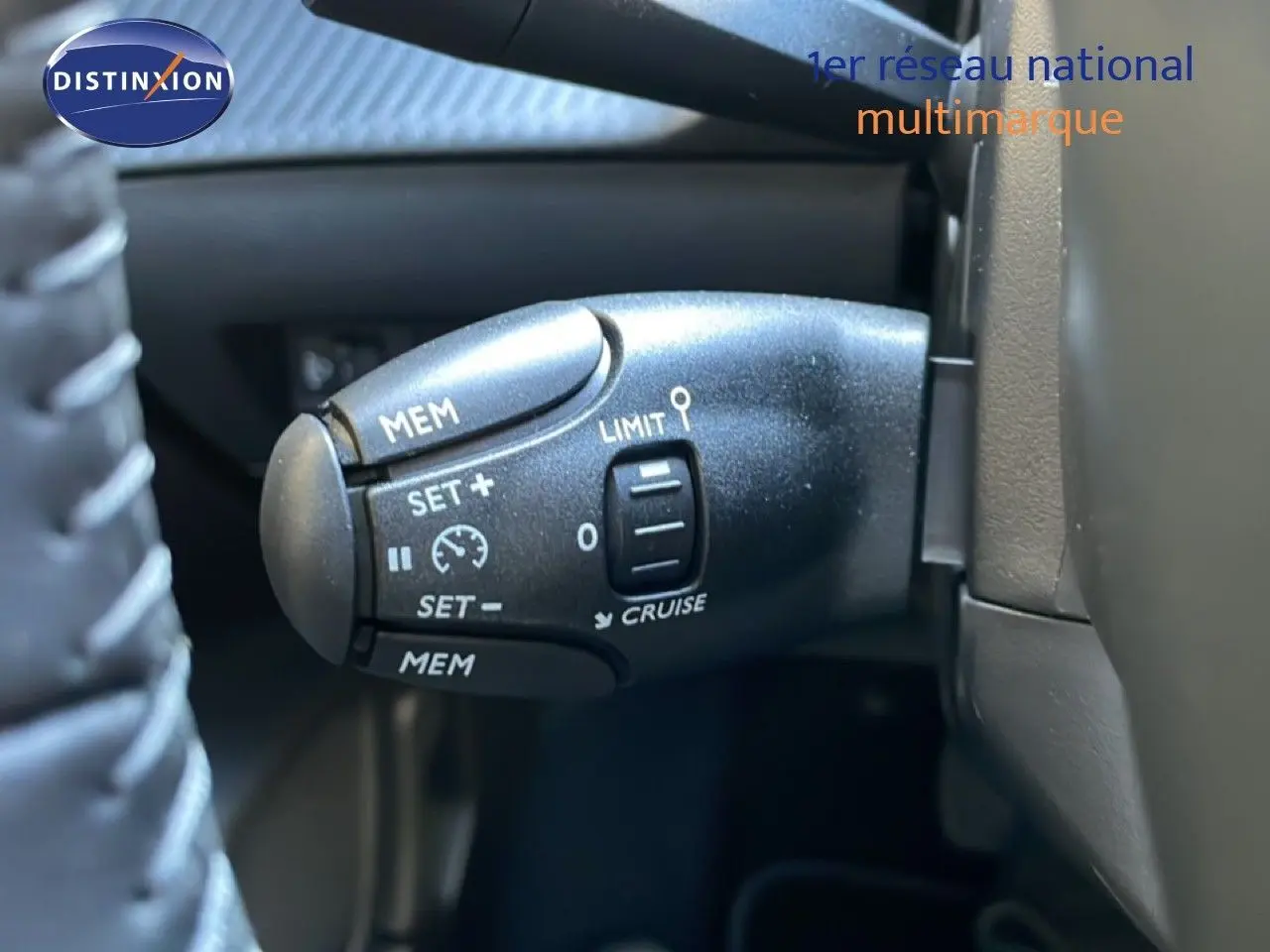 Gros plan sur la commande de régulateur de vitesse au volant d'une Peugeot 208 noire, version hybride 2026.