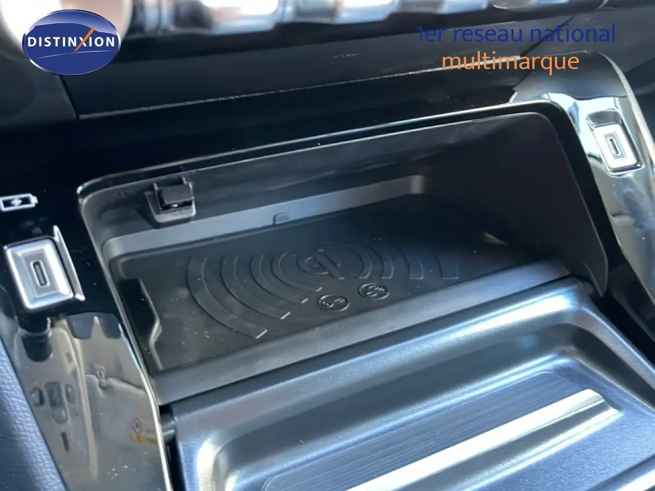 Détail de la console centrale noire perla metal de la Peugeot 208 Hybrid 110ch, avec zone de rangement et chargeur sans fil.