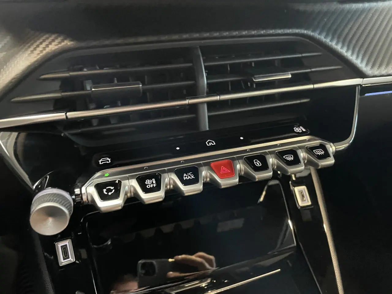 Gros plan sur la console centrale noire brillante du Peugeot 2008 bleu, avec boutons de commande et prises USB visibles.