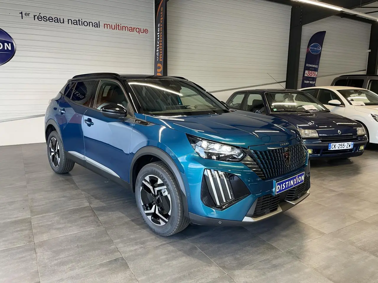 Peugeot 2008 1.2i Hybrid GT 2026 bleu, vue 3/4 avant avec calandre noire et toit noir brillant.