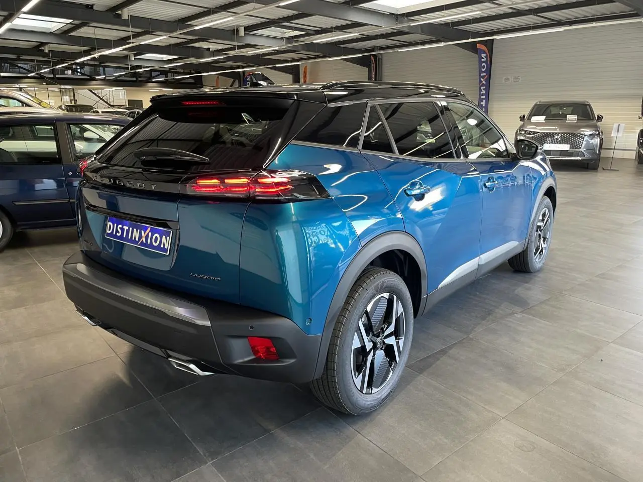 Peugeot 2008 hybride bleu vue 3/4 arrière droit en intérieur avec toit noir et feux arrière LED allumés.