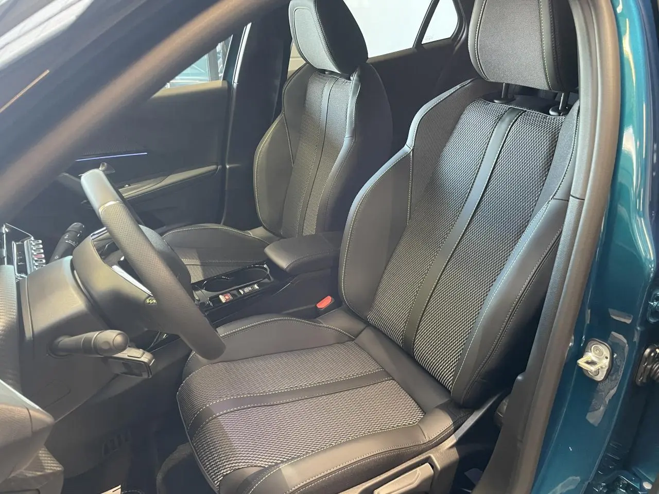 Vue intérieure côté conducteur du Peugeot 2008 bleu, mettant en valeur les sièges sport noirs avec surpiqûres contrastées.