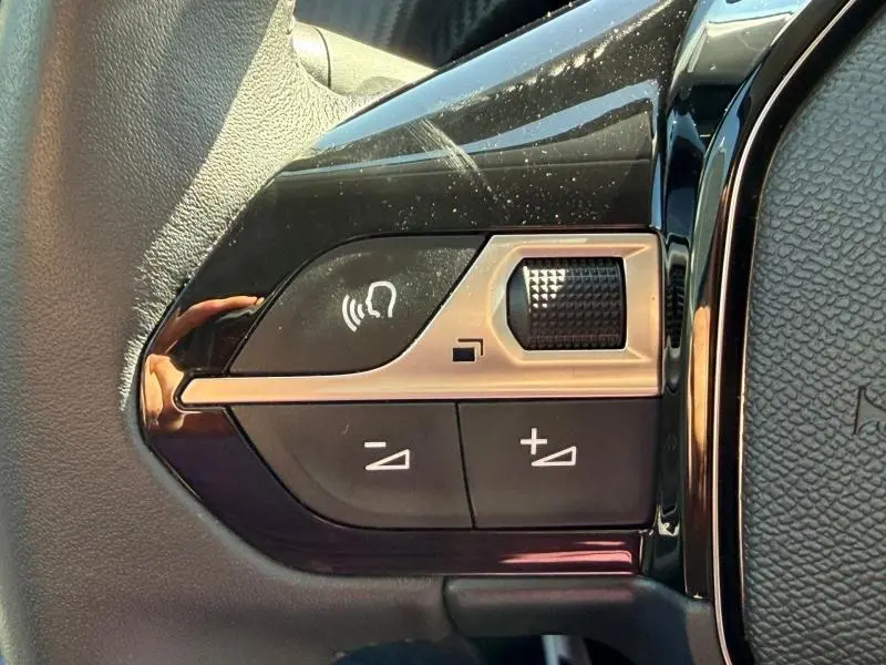 Gros plan sur les commandes vocales et de volume sur le volant noir de la Peugeot 208 1.2 100ch Allure.