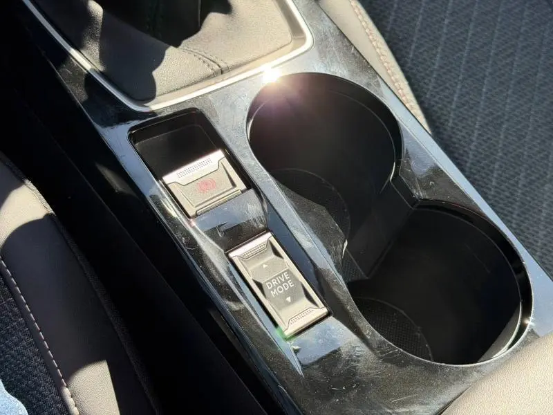 Gros plan sur la console centrale noire brillante de la Peugeot 208 blanche, avec commandes frein à main et mode de conduite.
