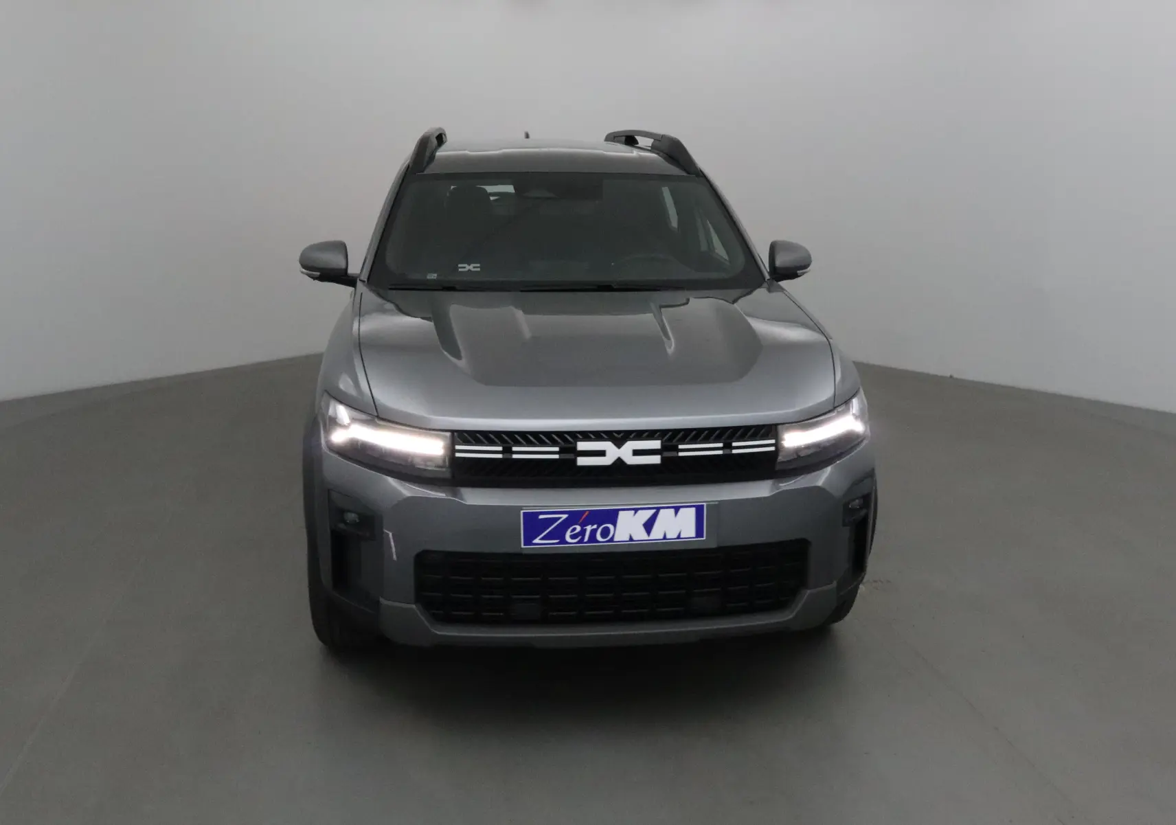 Vue frontale d'un Dacia Bigster gris schiste avec calandre noire et feux LED allumés dans un studio.