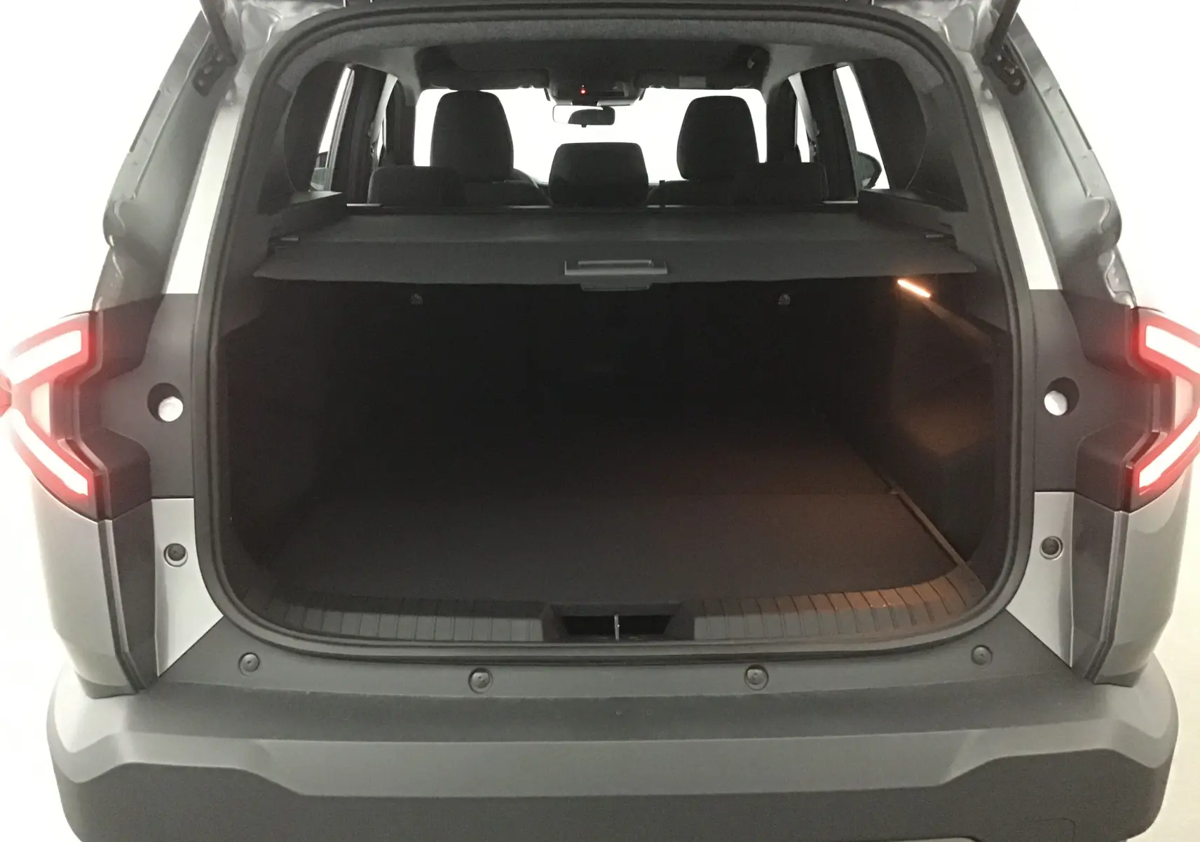 Vue arrière du coffre ouvert du Dacia Bigster gris schiste 2025, avec feux arrière allumés et banquette visible.