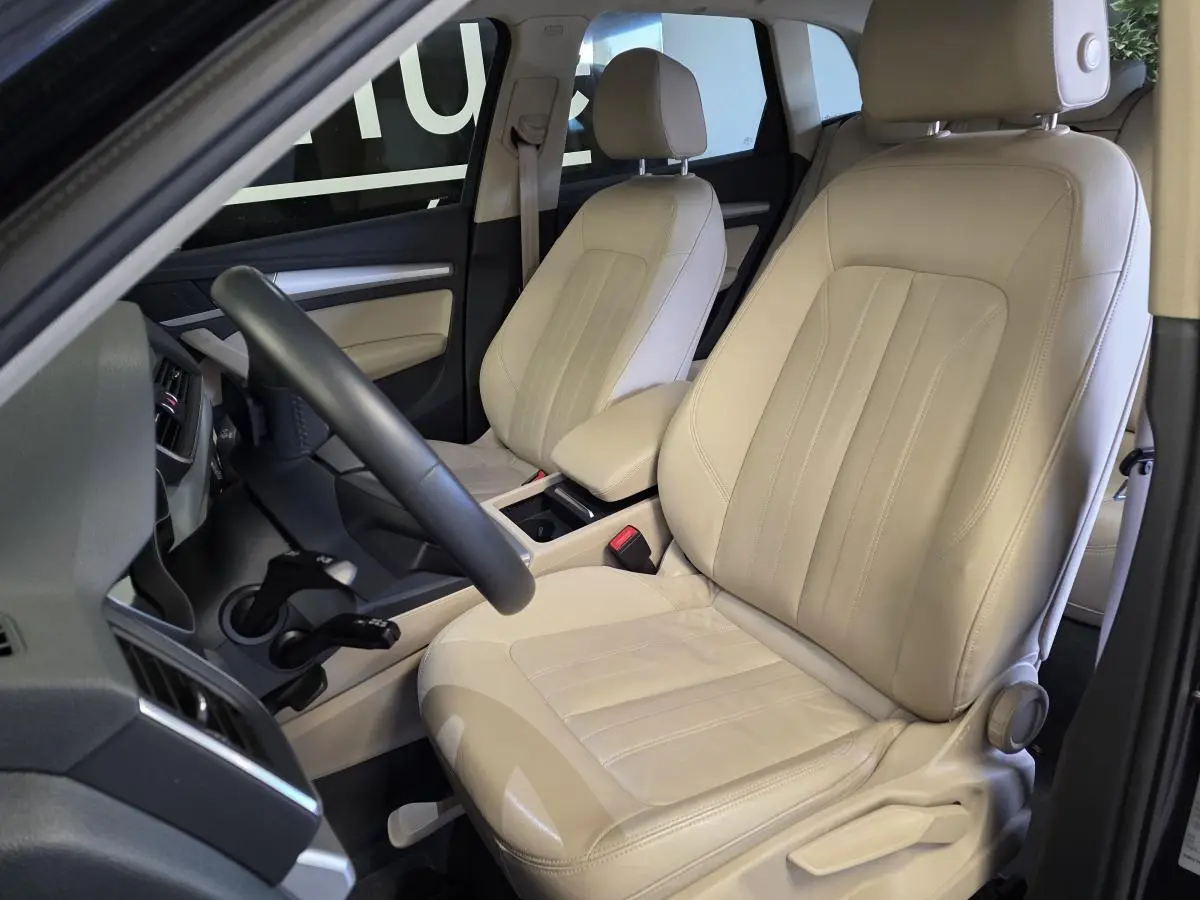 Intérieur Audi Q5 2019 vu côté conducteur, sièges cuir Milano beige avec accoudoir central et volant multifonction.
