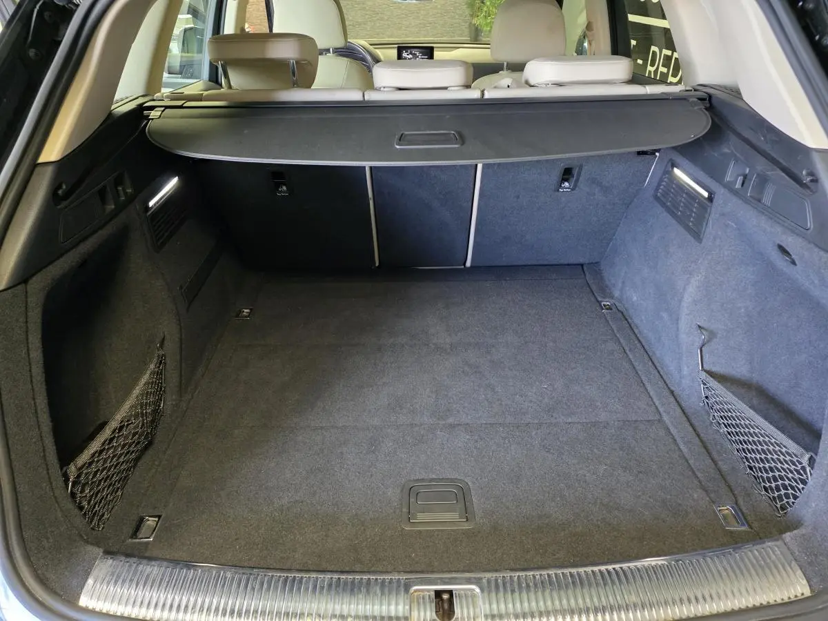 Coffre spacieux de l'Audi Q5 bleu 2019 vu de l'arrière, avec filet de rangement et cache-bagages noir.