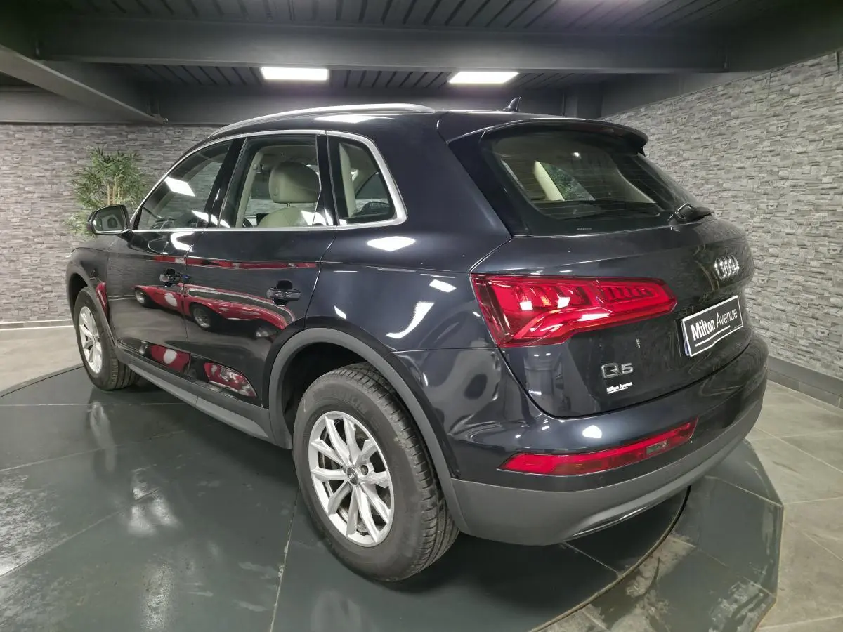 Audi Q5 bleu métallisé vu en 3/4 arrière côté gauche, avec feux arrière LED et jantes en alliage 17 pouces.