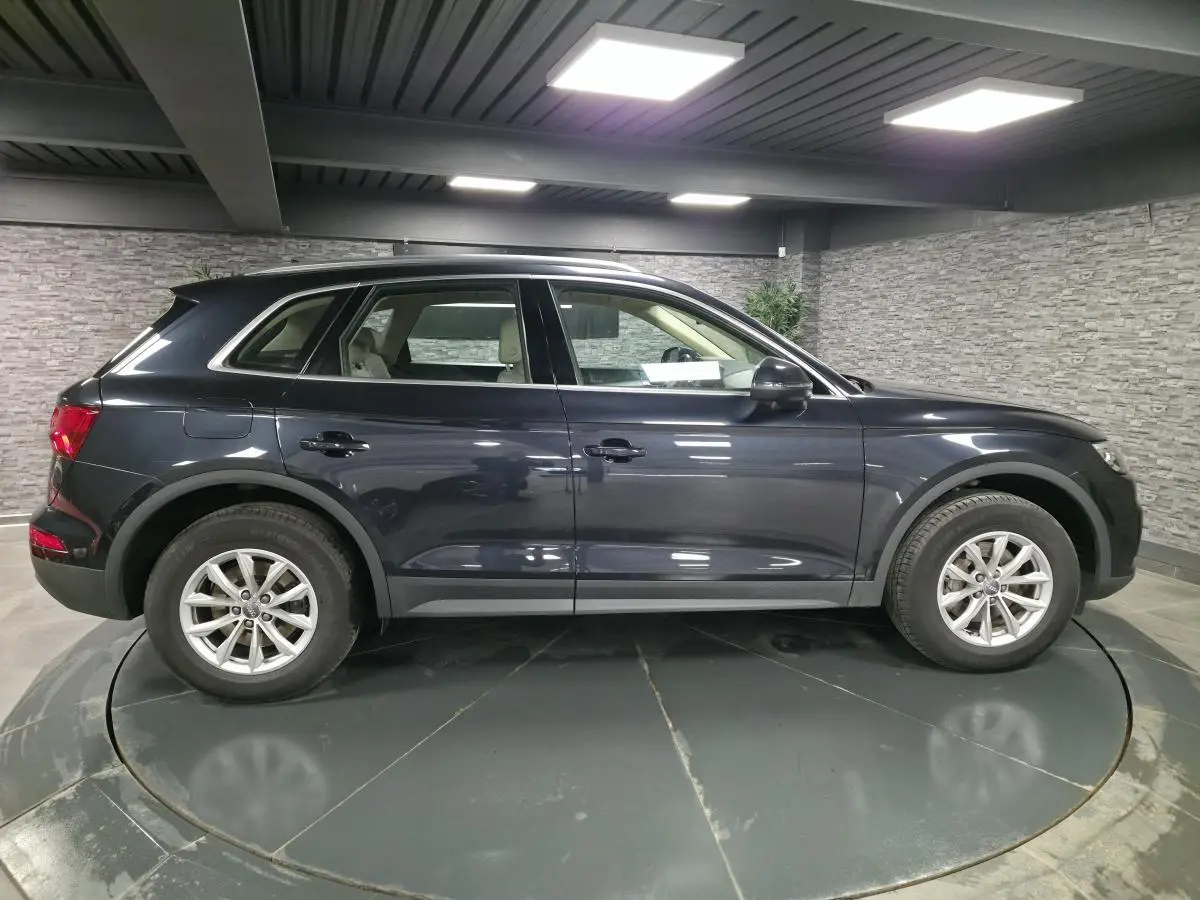 Vue de profil côté gauche d'un Audi Q5 bleu métallisé stationné en intérieur avec jantes aluminium à 10 branches.