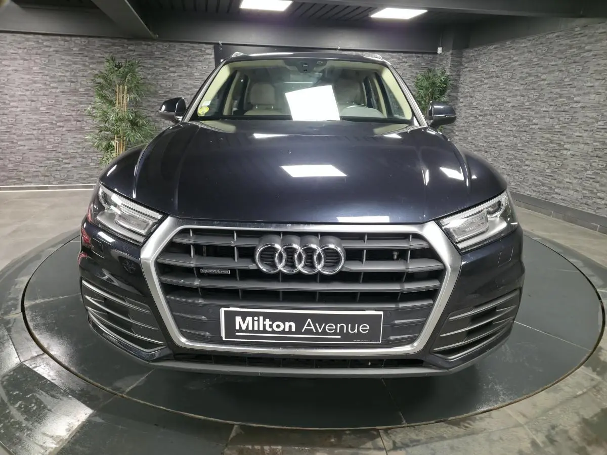 Vue frontale d'un Audi Q5 bleu métallisé avec calandre hexagonale et logo quatre anneaux bien visible.