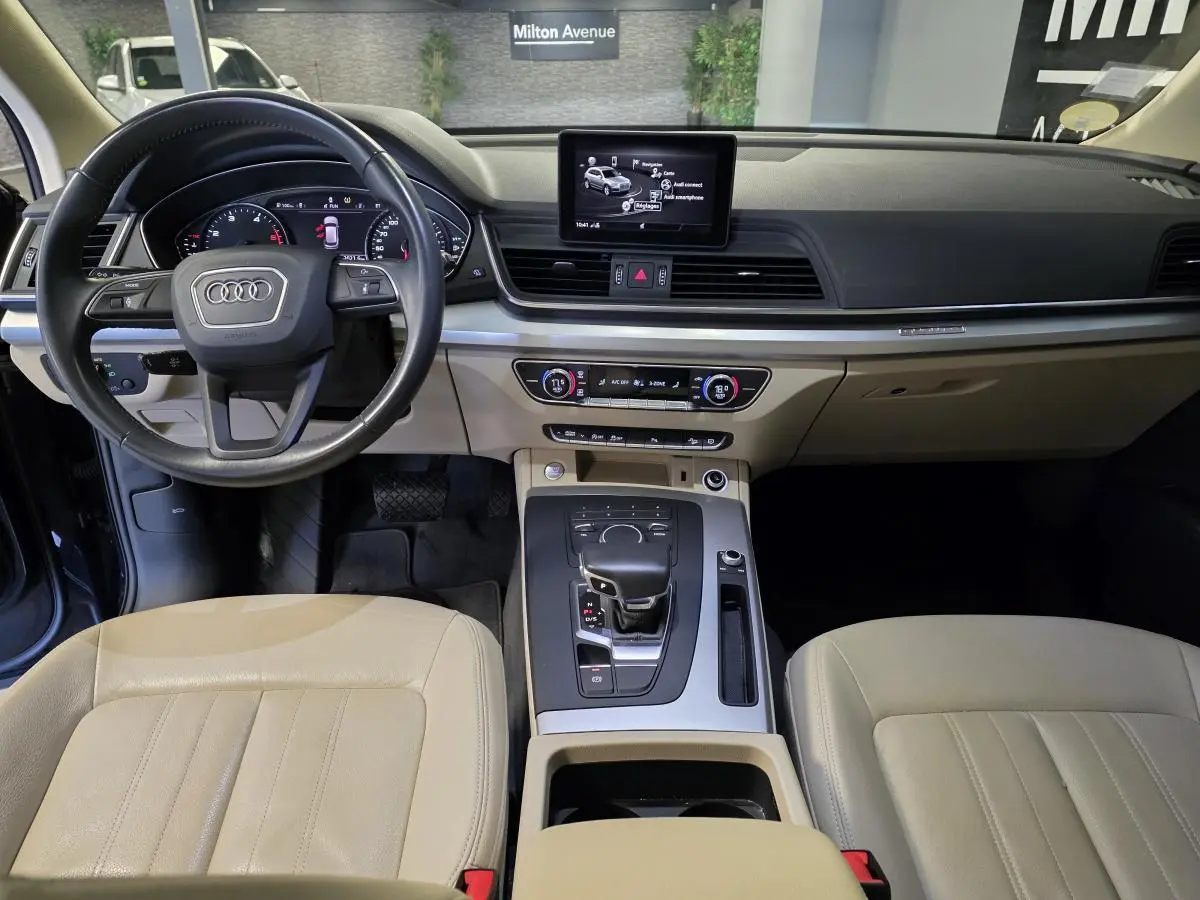 Vue intérieure de l'Audi Q5 2019 montrant le tableau de bord et la sellerie cuir beige avec console centrale moderne.