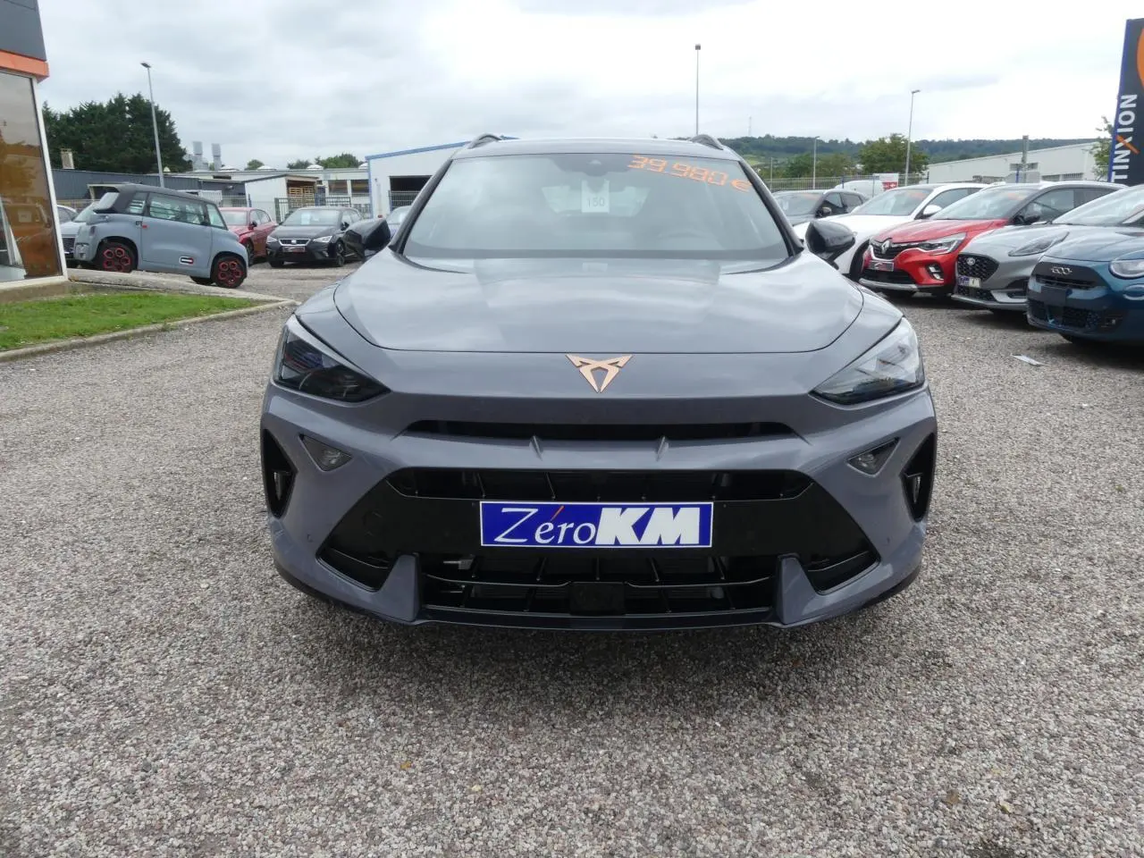 Vue frontale d'une CUPRA Formentor gris Graphène avec logo cuivré et calandre noire sportive sur parking.