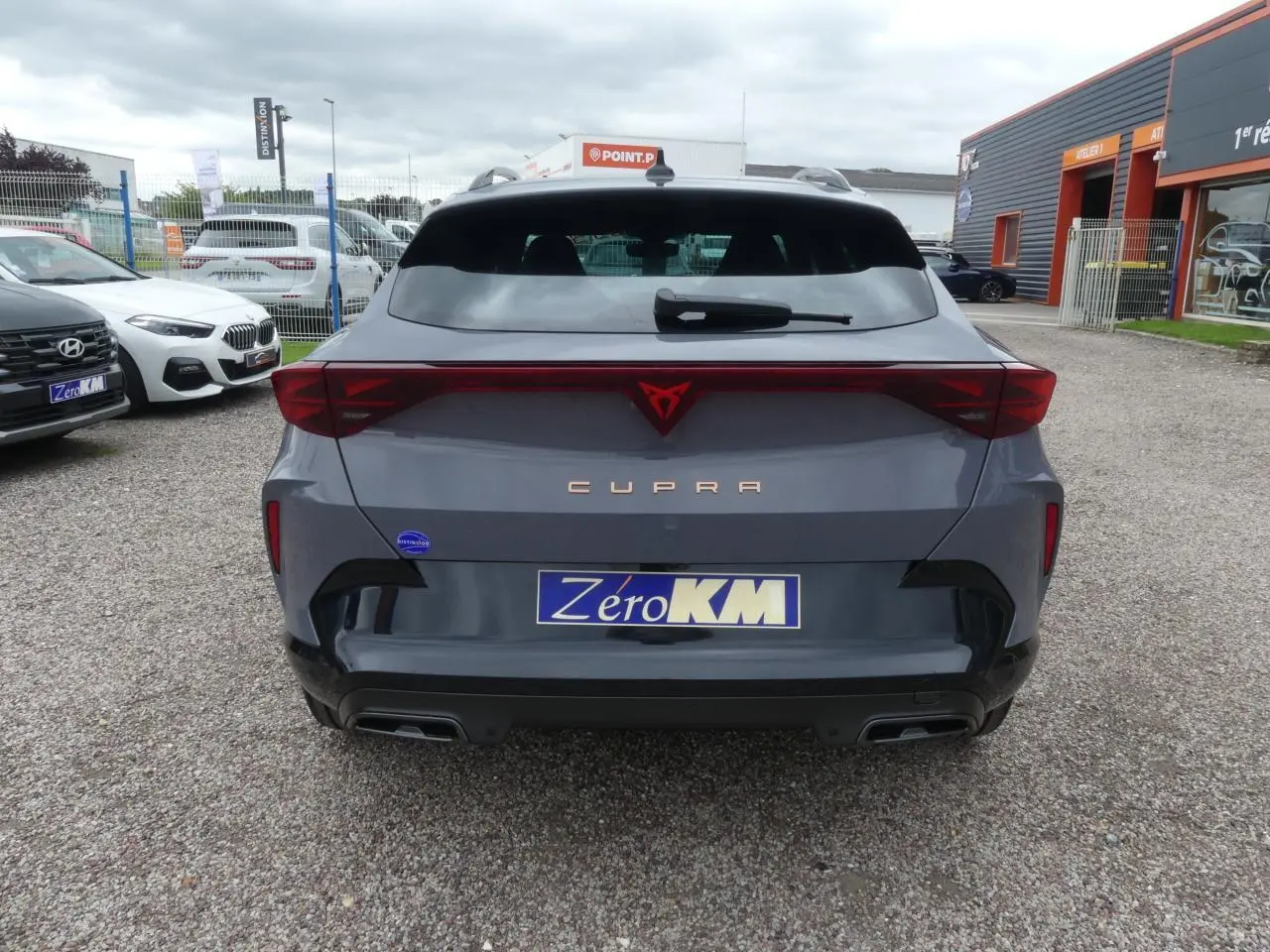 Vue arrière d'une CUPRA Formentor gris Graphène avec logo rouge et double sortie d'échappement noire sur parking.