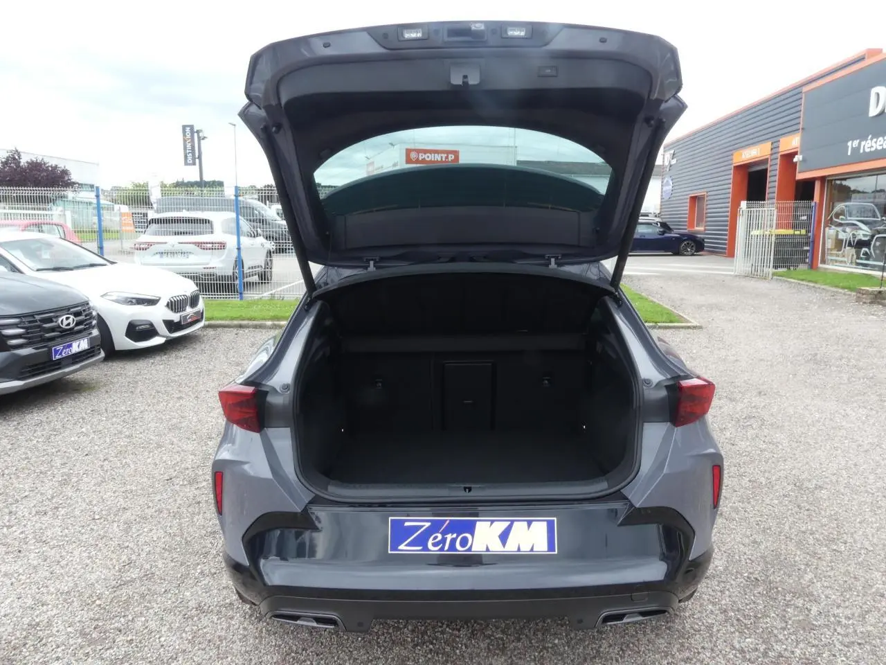 Vue arrière ouverte du coffre du CUPRA Formentor gris Graphène avec double sortie d’échappement et feux LED triangulaires.