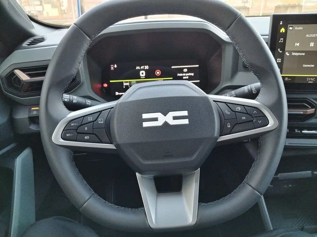 Vue rapprochée du volant noir du Dacia Bigster 2025 avec commandes intégrées et tableau de bord numérique allumé.