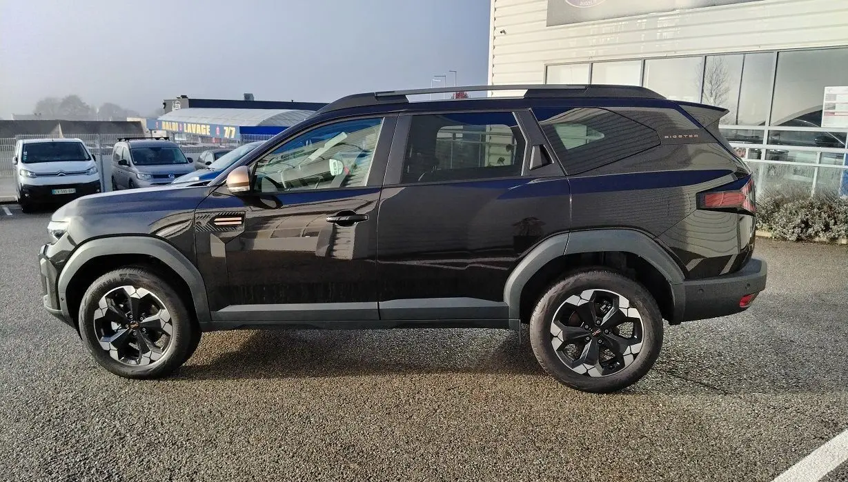 Profil côté gauche du SUV noir Dacia Bigster 2025 avec jantes bi-ton et toit surélevé, stationné en extérieur.